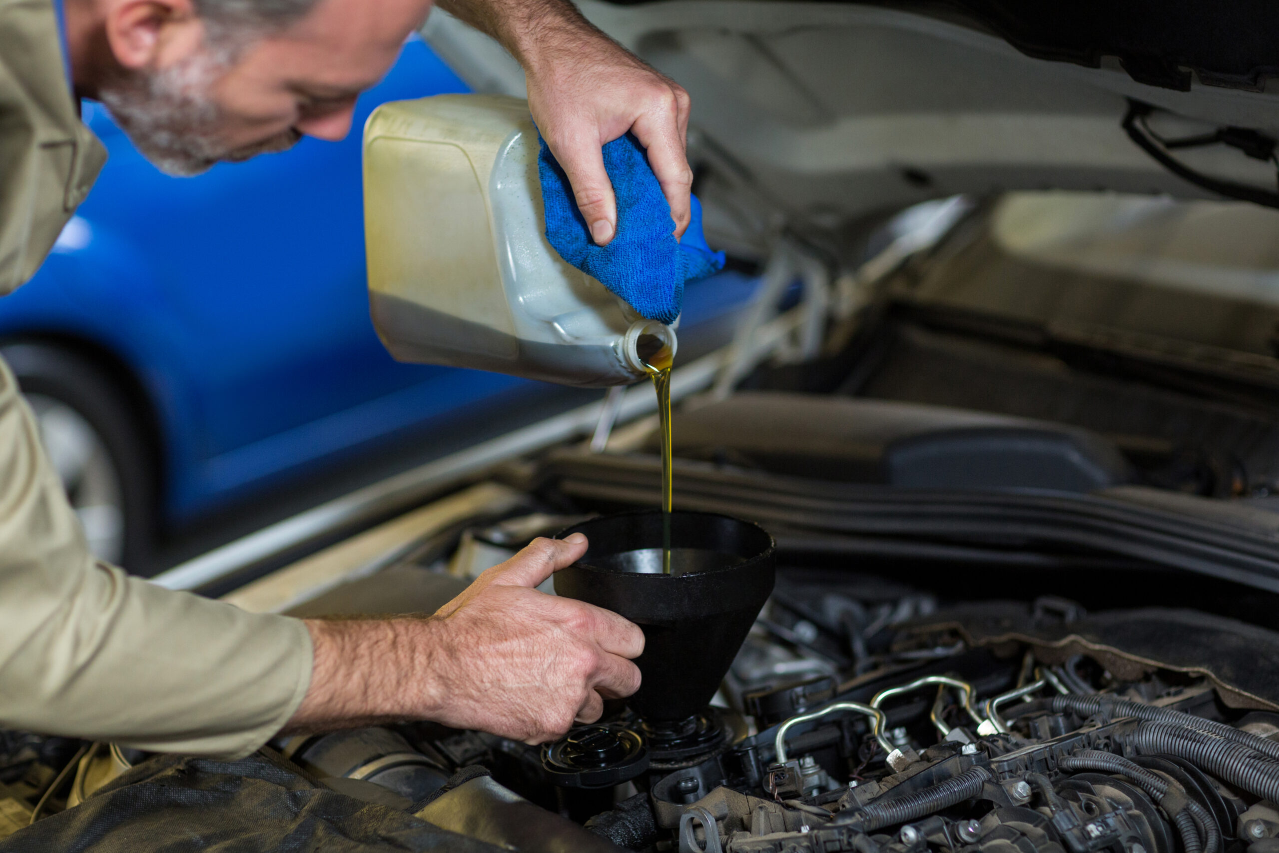 Mechanic pouring oil intoax car engine in repair garage